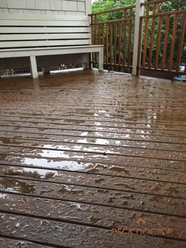 Water Beading On Freshly Stained Deck Floor With Bench And Rails In Background.